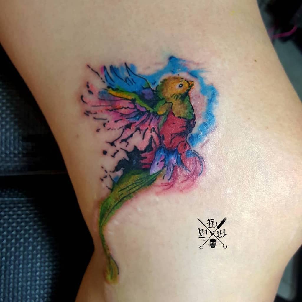 Quetzal bird tattoo with watercolor effects, showing wings spread wide in vivid hues of blue, red, and green