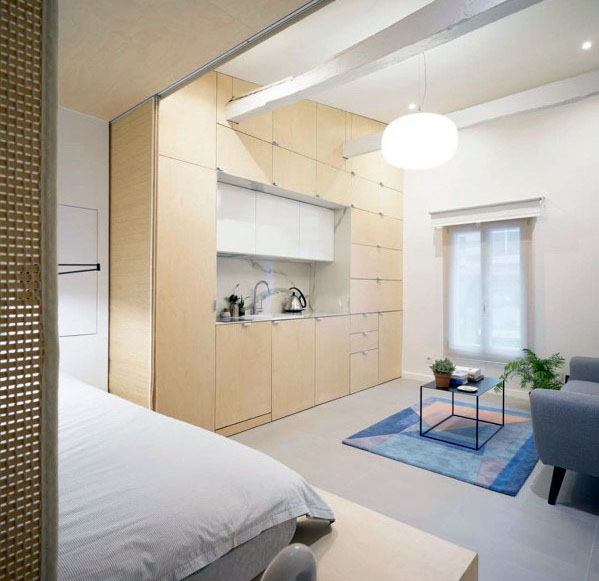 Minimalist studio with built-in wooden cabinetry, cozy bed, and compact living area.