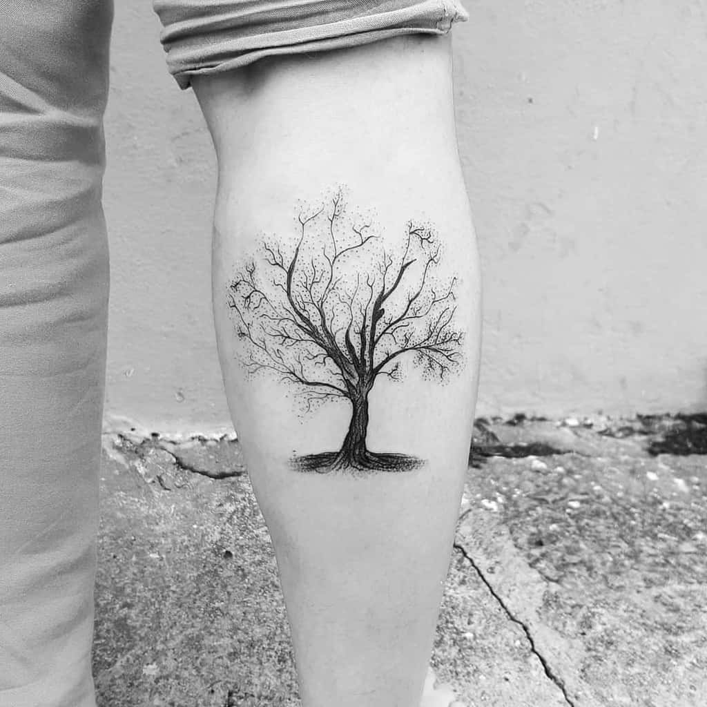 The tattoo showcases a minimalist tree design with delicate, branching limbs and fine details, capturing a serene, natural aesthetic.