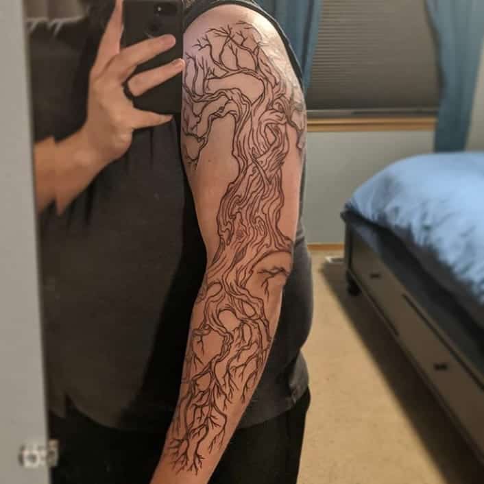 This full-arm tattoo features an intricate tree with twisting branches and roots, symbolizing growth, strength, and resilience.
