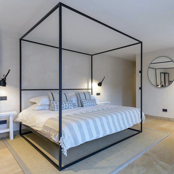 Minimalist bedroom with a black four-poster bed, white modern linens, wall-mounted lamps, and a round mirror on the wall