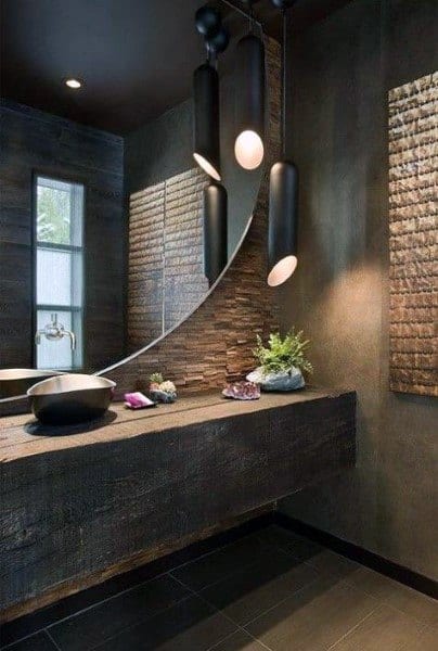 Modern bathroom with curved mirror, pendant lighting, and dark textured walls.