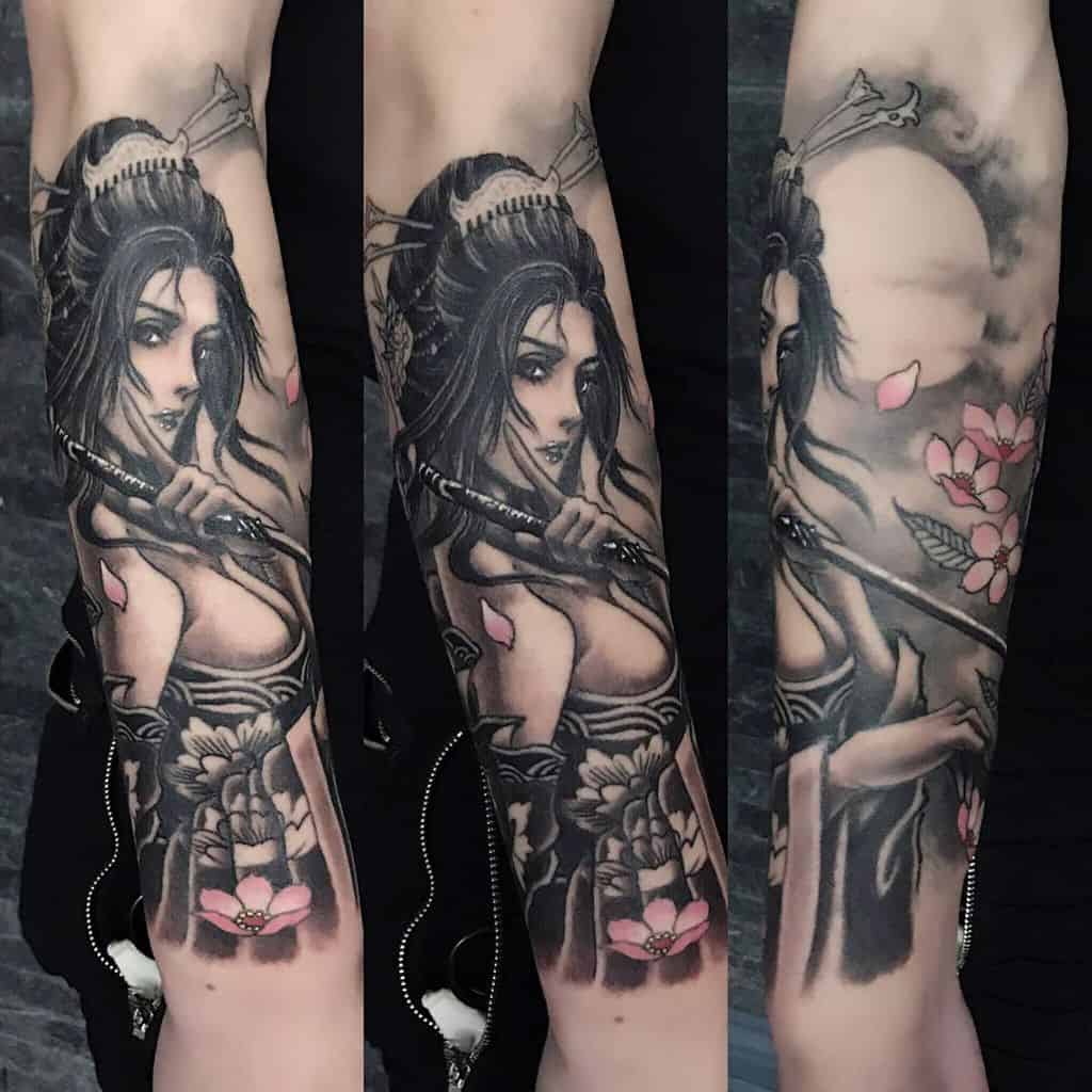 Black and gray forearm tattoo of a warrior Geisha holding a katana, with pink cherry blossoms, intricate shading, and a glowing full moon backdrop.