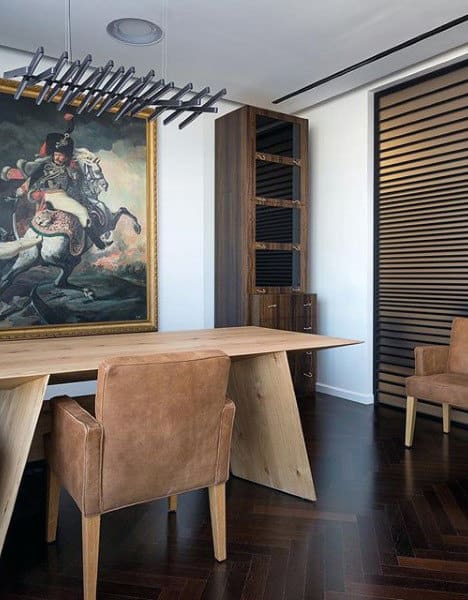 Modern office with a wooden desk, two brown chairs, a large painting, and a stylish ceiling light fixture