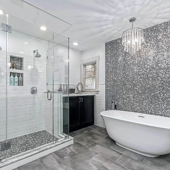 Modern bathroom with freestanding tub, glass shower, gray mosaic wall, and chandelier.