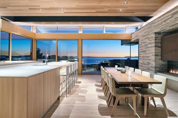 Modern open-concept kitchen and dining area with wood ceiling, stone fireplace, and sleek furniture.