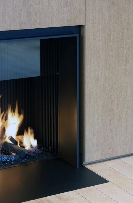 Minimalist modern fireplace with black metal accents and wood paneling.
