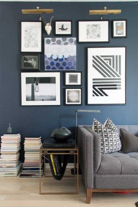 Gallery wall of modern framed art in various styles above a gray sofa and side table.