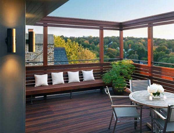 Rooftop patio with wooden furniture and a bench, a potted plant, and a scenic view of trees in the background