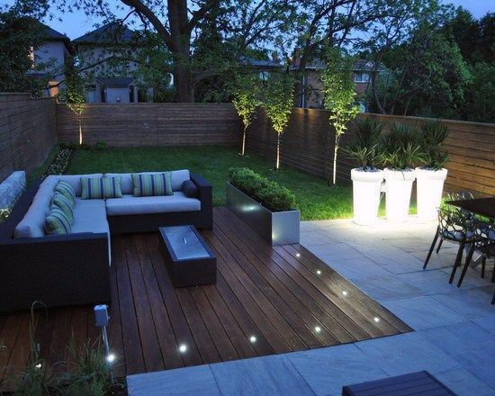 Contemporary backyard deck with sectional sofa, LED lights, and lush greenery.