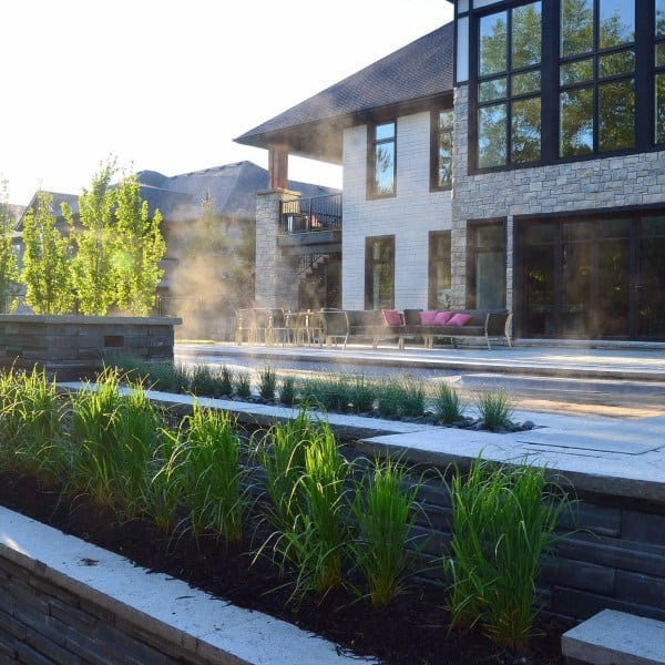 Modern backyard with tiered planters, patio seating, and mist effects near a luxury home.