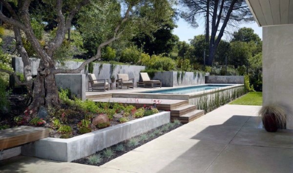 Modern backyard with a pool, concrete planters, wooden steps, and lush greenery.
