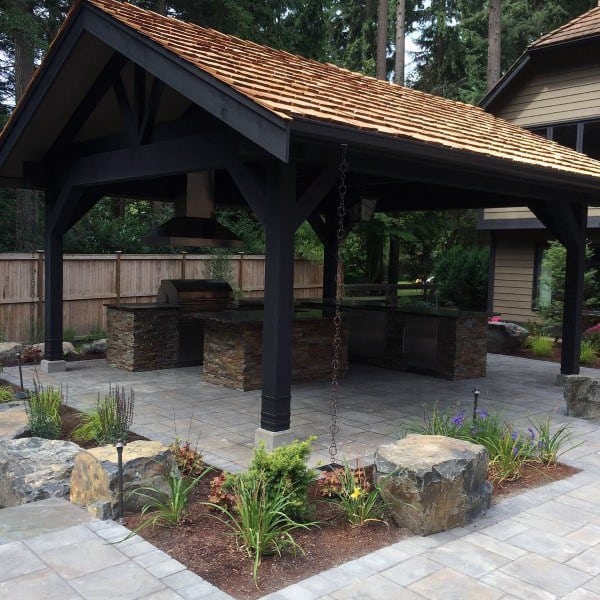 Modern pavilion with a wooden frame, outdoor kitchen, stone countertops, and a cedar shingle roof.