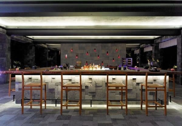 Modern bar with backlit counter, three wooden stools, and wall lighting, creating a sleek bar ambiance