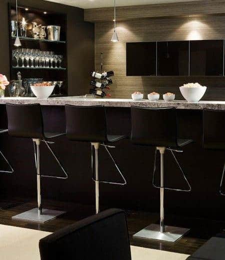 Modern kitchen bar with black stools, hanging glasses, and a wine rack, featuring a counter filled with decor