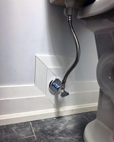 Bathroom baseboard with cutout for plumbing and gray tiled flooring.