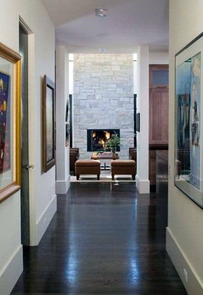 Hallway with dark wood floors, white walls, and a stone fireplace at the end.
