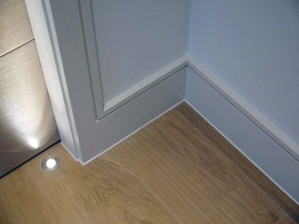 Corner detail with gray baseboard, door trim, and light wood flooring.