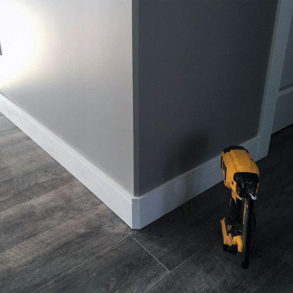 Gray wall with white baseboard molding and gray textured flooring.