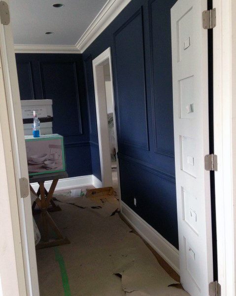Narrow hallway with navy blue paneled walls, white baseboards, and crown molding.