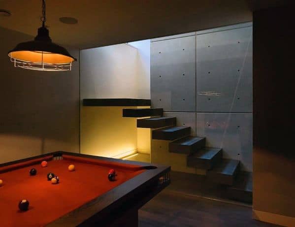 Modern billiard room with red felt pool table industrial lighting and floating staircase.
