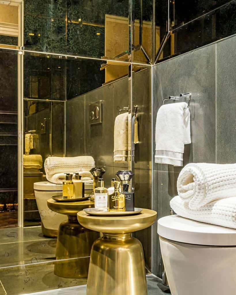 Luxurious bathroom with mirrored walls, gold stool, and modern fixtures.