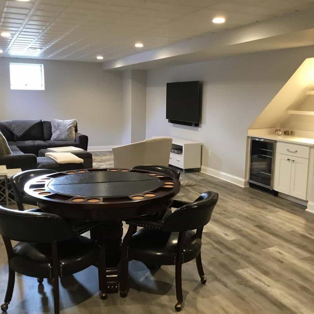Simple basement area with a living space, poker table, and a small kitchenette.