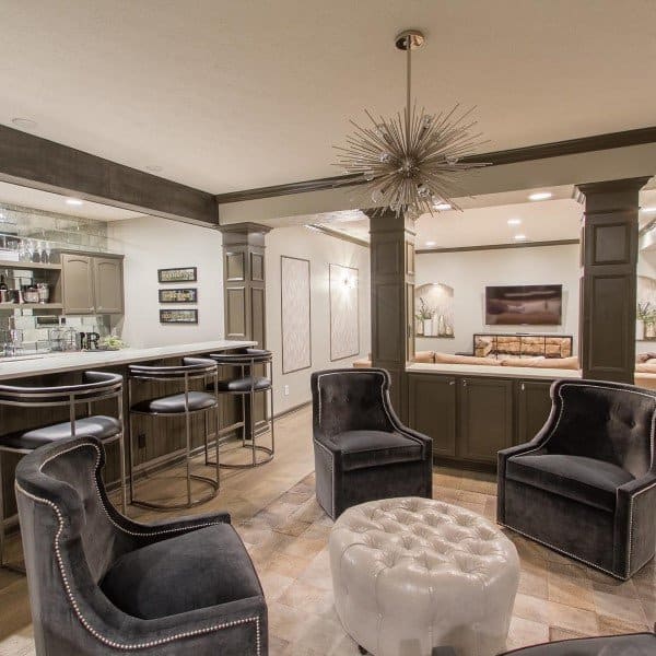 Modern basement with bar area, velvet seating, tufted ottoman, and crystal chandelier.