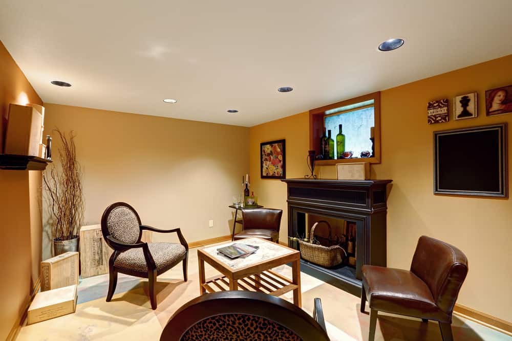 Modern basement living room with cozy fireplace, leather chairs, and warm-toned walls.