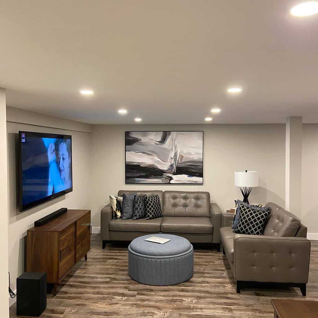 Modern basement lounge with gray leather couches, mounted TV, and abstract wall art.