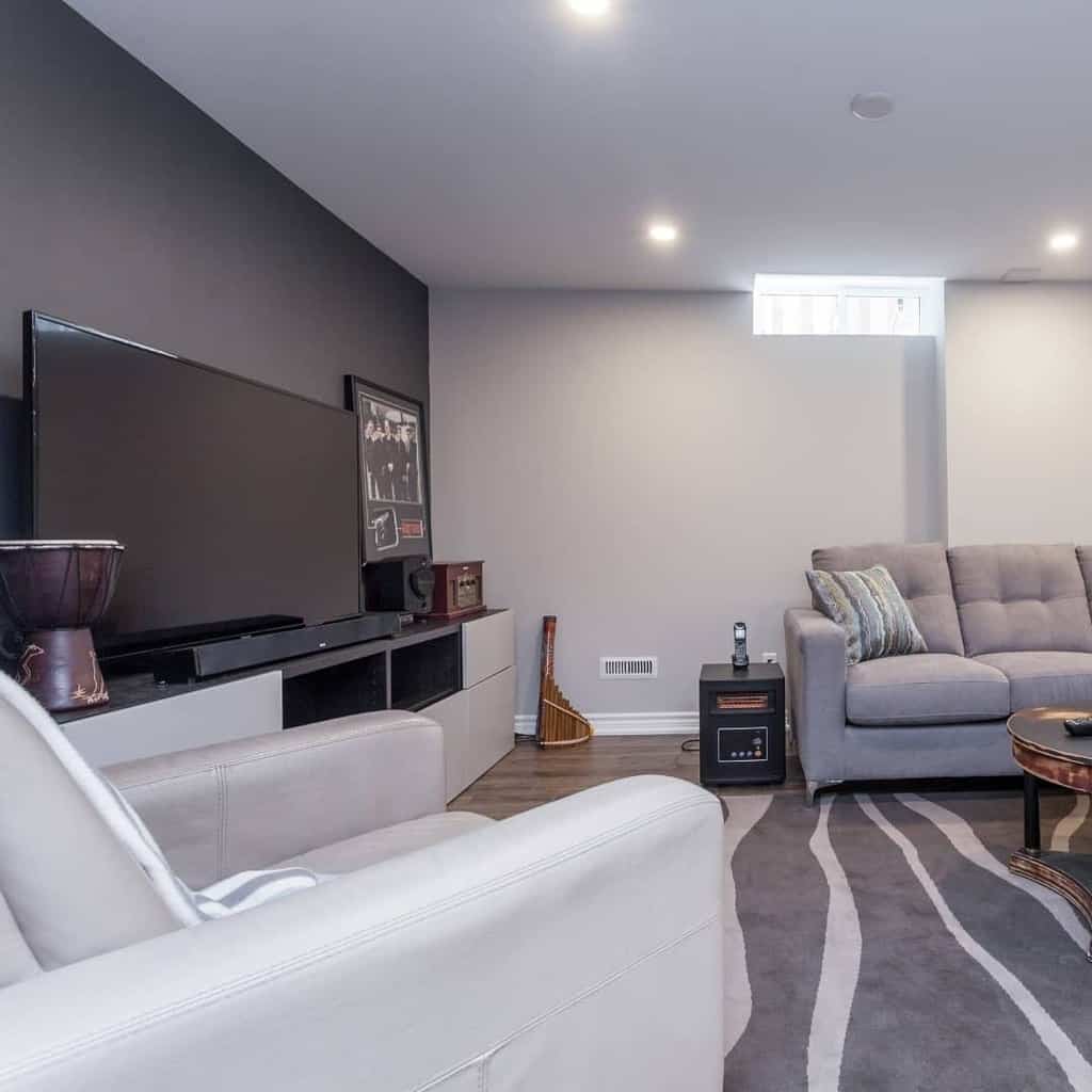 Contemporary basement living space with gray sectional sofa, large TV, and modern decor.