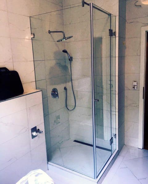 Corner glass shower enclosure with a rainfall showerhead and handheld sprayer in a tiled bathroom