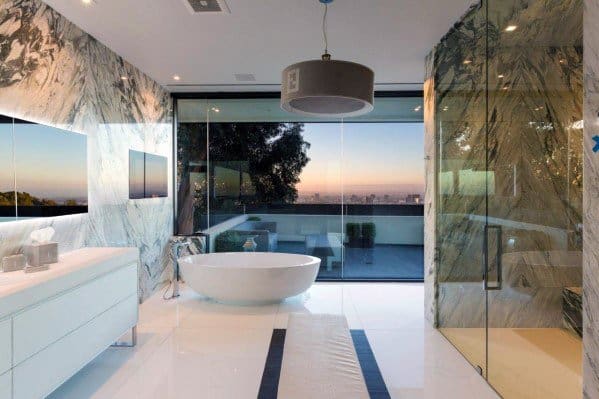 Luxury bathroom with freestanding tub, marble walls, glass shower, and large window view.