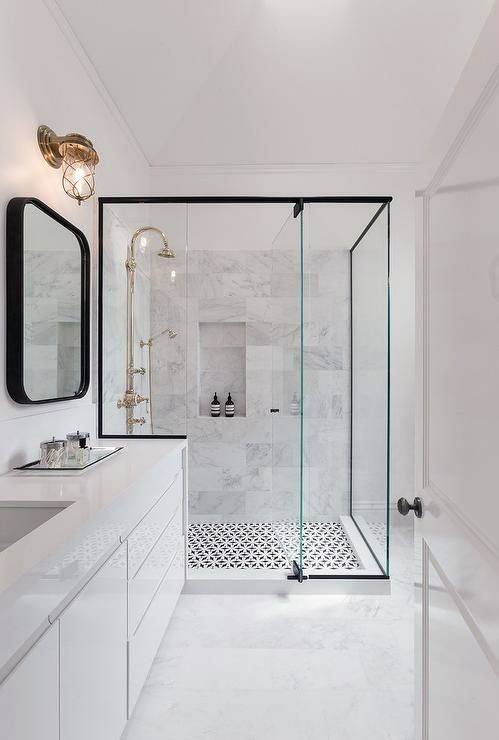 Bright bathroom with glass shower, patterned tile floor, and gold fixtures.