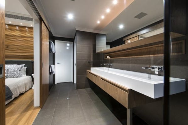 Modern bathroom with a long double sink, large mirror, and sliding door leading to bedroom