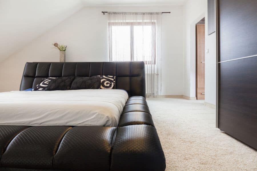 Modern bedroom with black leather bed frame, white bedding, and minimalistic decor.
