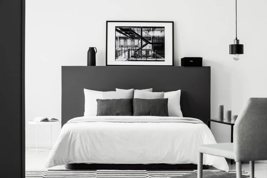 Minimalist bedroom with black headboard, white bedding, framed black-and-white artwork, and pendant light.