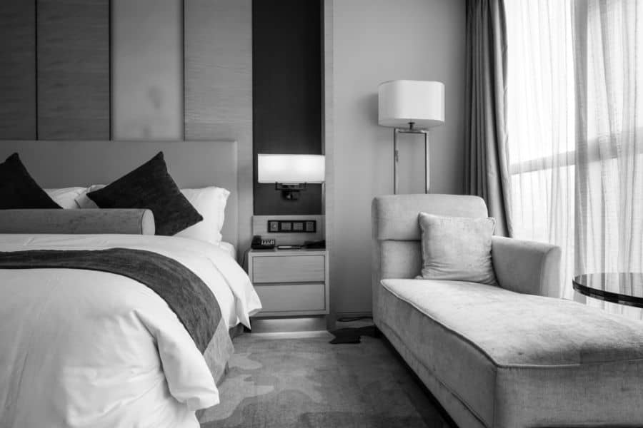 Modern black and white bedroom with upholstered headboard, chaise lounge, and floor lamp.