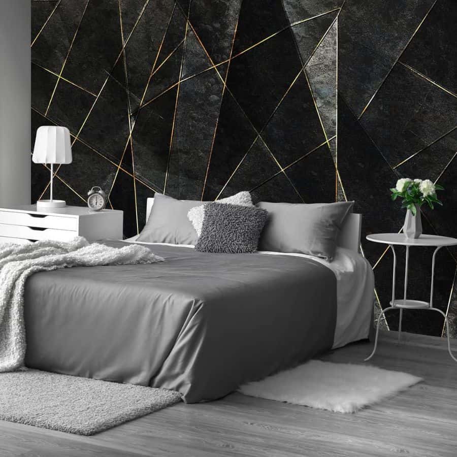 Modern bedroom with geometric black accent wall, gray bedding, and white furniture.