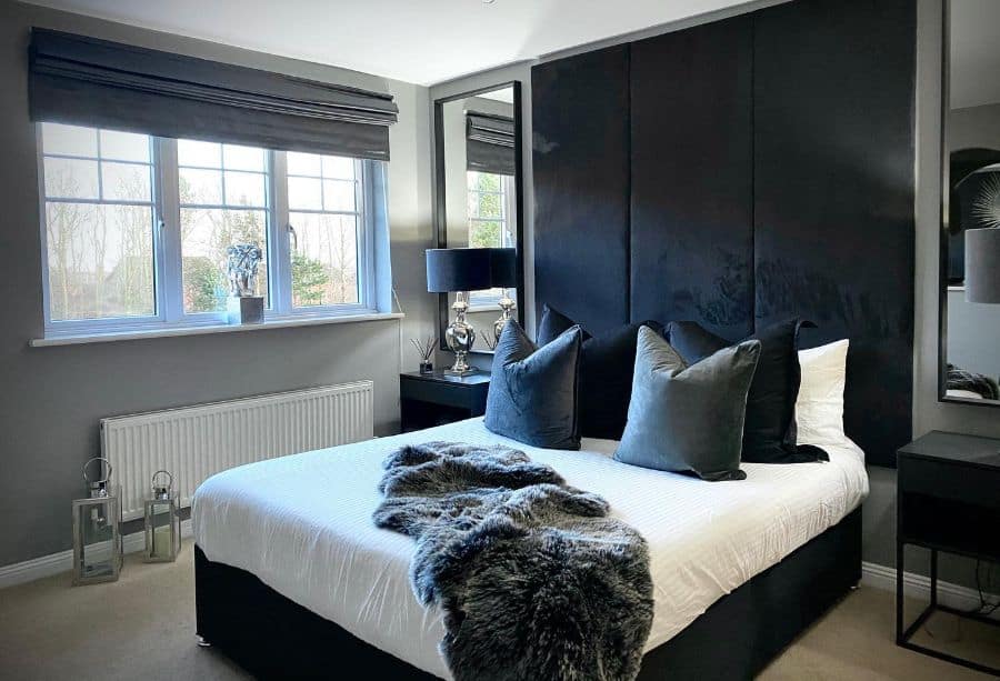 Modern bedroom with black paneled wall, gray pillows, and white bedding with faux fur throw.