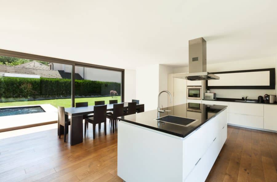 Modern black and white kitchen with island, dining table, and garden view through glass.