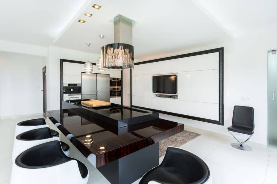 Modern kitchen with black glossy island, white cabinets, bar stools, and built-in TV.