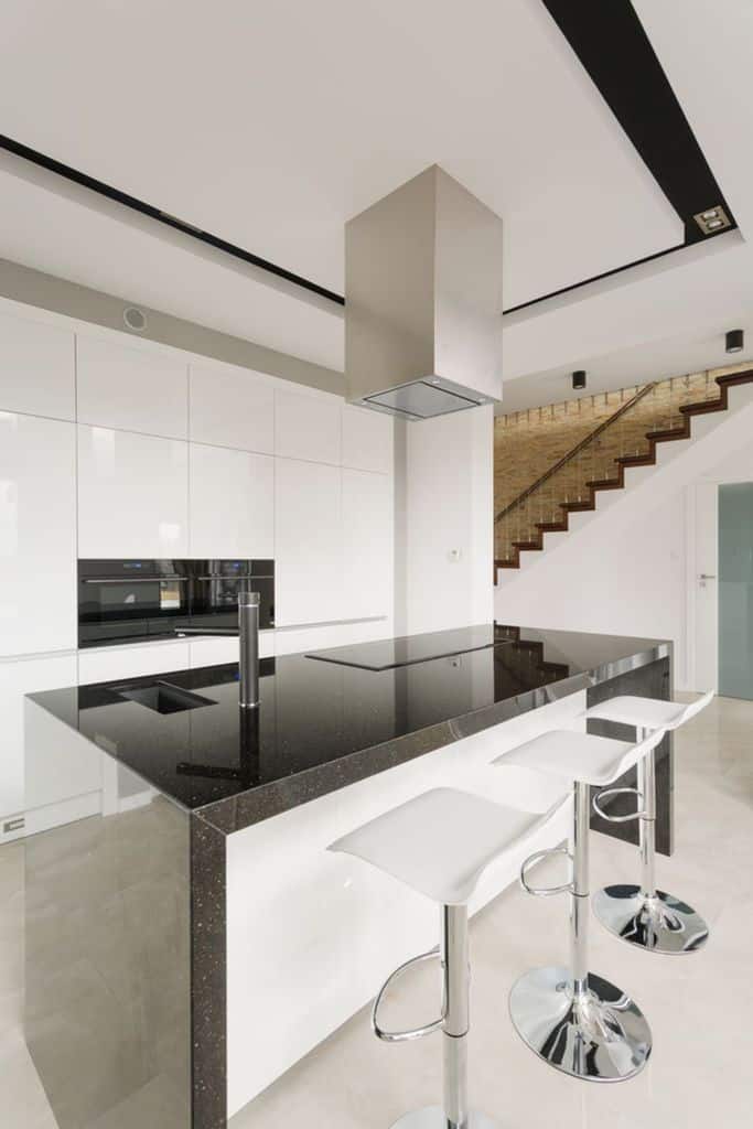 Modern kitchen with black countertop island, white bar stools, and built-in appliances.