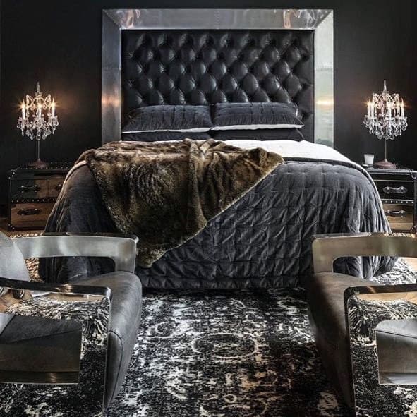Luxurious black bedroom with tufted headboard, fur throw, chandeliers, and modern chairs.