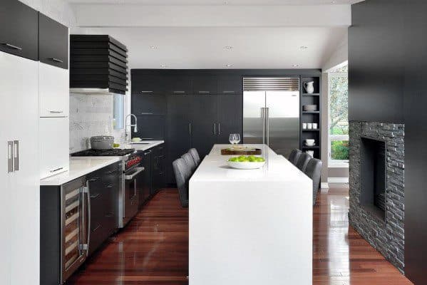 Modern black kitchen with white island, dark cabinets, wood floors, and stone fireplace.