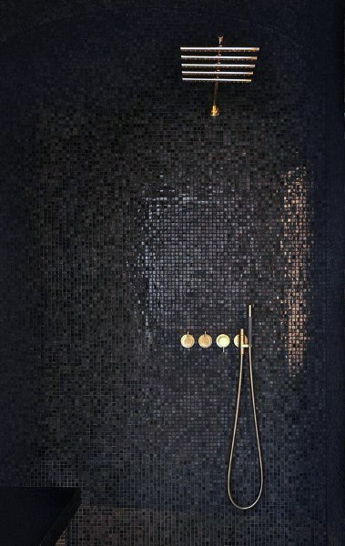 Black mosaic tile shower with brass fixtures and a rainfall showerhead.