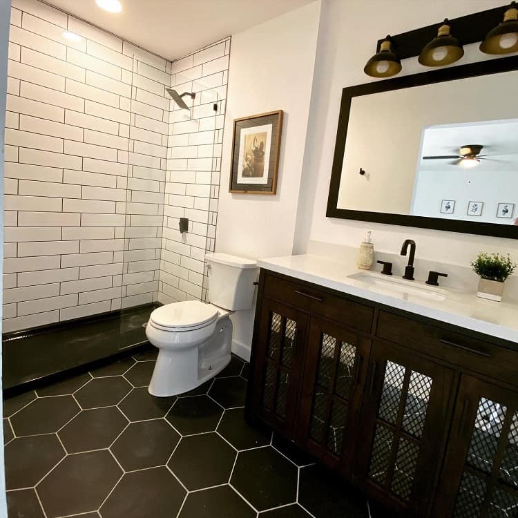 Modern farmhouse bathroom with black hexagon tile floor, white subway shower tiles, and wood vanity.