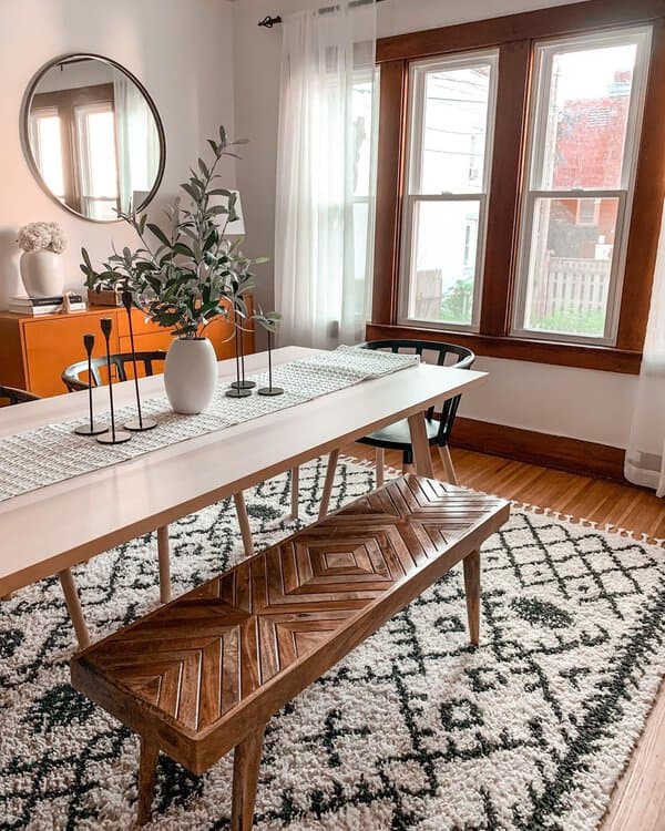 Modern boho dining room with sleek table, wooden bench, and greenery accents.