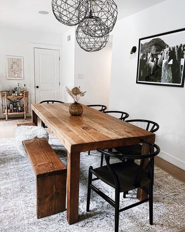 Modern boho dining room with rustic wooden table, black chairs, and geometric pendant lighting.