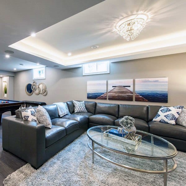 Modern basement with recessed ceiling lighting, a crystal chandelier, sectional sofa, and decor.